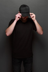 Hipster handsome male model with beard wearing black blank t-shirt and a black baseball cap with space for your logo or design in casual urban style