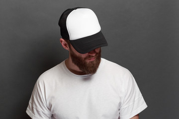 Hipster handsome male model with beard wearing white blank t-shirt and a baseball cap with space for your logo or design in casual urban style