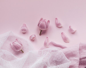 Pink tulip heads and flower petals next to white and pink fabrics isolated on light pink background. Flat lay. Copy space. Top view