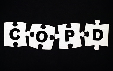 Four pieces of puzzle with letters COPD. Black background