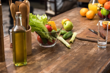 close-up view of fresh vegetables in glass bowl, oil in bottle and wooden kitchen utensils on table