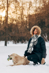 Photo of smiling girl with labrador on background of trees in winter park