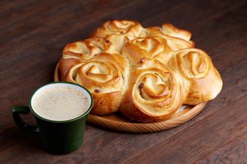 Creamy coffee in cup with homemade rose bread on vintage wooden background, close-up, selective focus