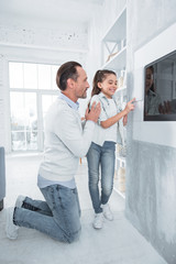 Do not worry. Nice positive handsome man standing near his daughter and helping her while teaching how to use smart home technology