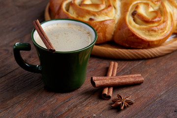 Creamy coffee in cup with homemade rose bread on vintage wooden background, close-up, selective focus