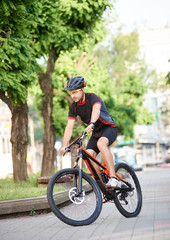 Obraz premium Young male cycler in cycling sportswear and protective gear performing tricks on city streets, getting ready for contest. Cyclist training, improving skills, reaching goal. Concept of motivation