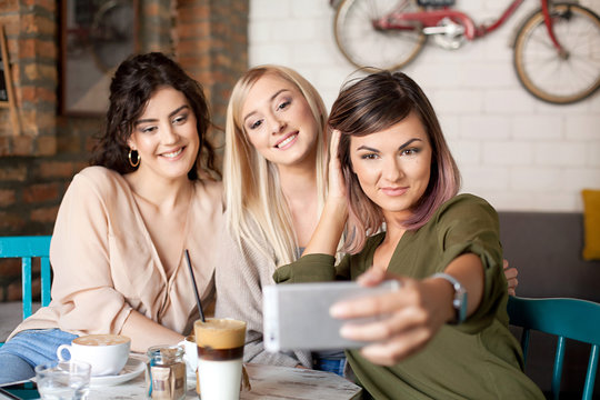 Female Friends In Cafe Taking Selfie Using Smart Phone. Women smiling, having fun, drinking coffee, laughing and enjoying their time.