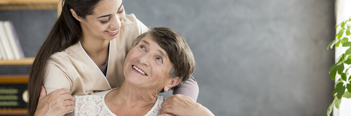 Friendly caregiver hugging senior woman