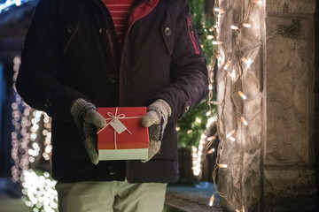 Close up of Christmas box in man hands with gloves, outdoors. Christmas and winter holidays concept.