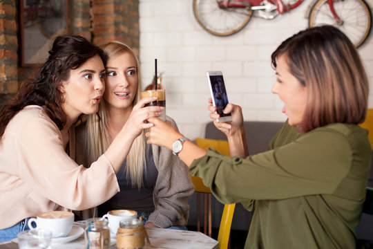Female friends making a toast with coffee. Women at cafe celebrating, relaxing, laughing and enjoying their time. One woman making a picture of other two.