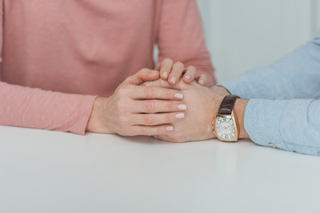 partial view of mother and grown son holding hands while sitting at table