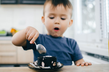 A small child eats a black chocolate cake, at home in the kitchen