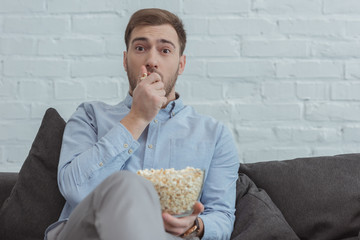 portrait of scared man with popcorn watching film at home