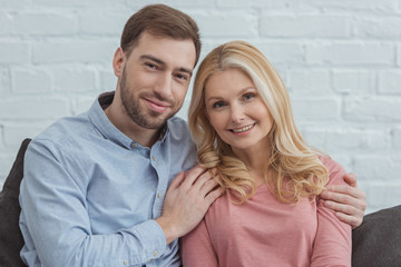 Fototapeta premium portrait of smiling son hugging mother while resting on sofa at home
