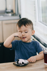 A small child eats black chocolate cake, at home in the kitchen next to the red juice of...