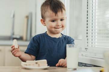 Naklejka premium a little charming boy eats waffles in the kitchen and drinks milk