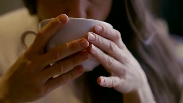 middle-aged woman sitting in a cafe with a Cup of tea or coffee and swallowing. Close-up of hands with a Cup