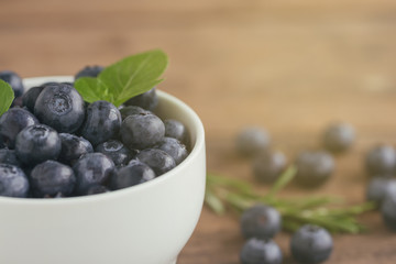 Fresh blueberries heap on white bowl in close up view under sunlight with copy space on wood table for background. Blueberry is healthy and delicious fruits which have high antioxidant and vitamin C.