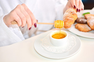 The girl in a white bathrobe eats home croissants with honey. The anticipation of taste concept.