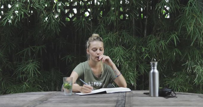 awesome blond beautiful girl or woman (creator, student, artist, writer) working on nature outdoors, wriring in her album or book, checking phone for messages (wifi, internet, worldwide, downshifting)