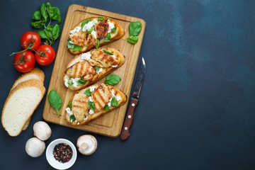Delicious traditional bruschetta with grilled chicken, ricotta and basil on dark backdrop. Food background for Italian restaurant or menu