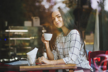 Beautiful young brunette sitting in a cafe and drinking tea.