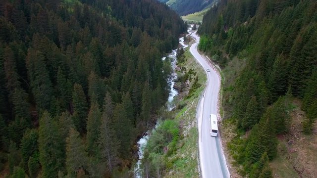Aerial view of driving white color bus by a road in a mountainous area between the pine forest in Austria.