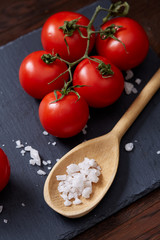 Vegetarian still life with fresh grape tomatoes, pepper and salt in wooden spoon on wooden background, selective focus