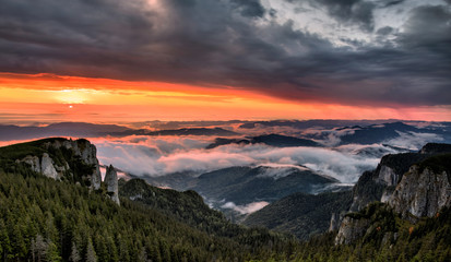 Naklejka na ściany i meble Panorama of a beautiful mountain view with fog over the peaks at sunrise, Ceahlau massif, Eastern Carpathians, Moldova, Romania