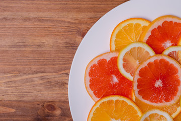 orange grapefruit and lemon cutting into a plate on a wooden background