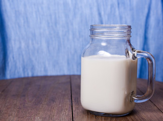 milk in a jug and a glass on blue blackground  on wooden table.