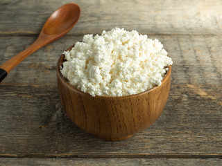 Homemade cottage cheese in a wooden bowl with a spoon on a rustic wooden table.