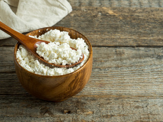 Homemade cottage cheese in a wooden bowl with a spoon on a rustic wooden table.