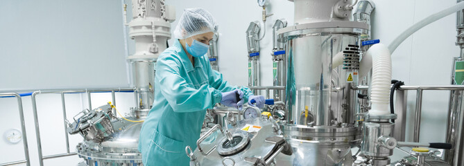 Pharmaceutical factory woman worker in protective clothing operating production line in sterile...