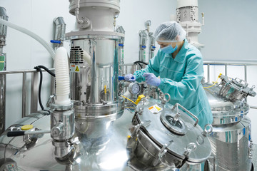 Pharmaceutical factory woman worker in protective clothing operating production line in sterile...