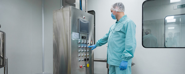 Pharmaceutical factory man worker in protective clothing working with control panel in sterile...