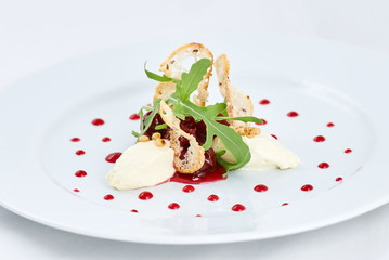 Delicious dessert. White three pieces of ice cream with strawberry and green leaves of arugula, and and thin rusks in the centre of a plate with dots of strawberry jam.