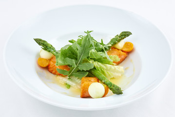 Delicious salad. Tasty dish with pieces of grilled salmon, cheese, orange tomatoes, green leaves of arugula and asparagus on a white plate.