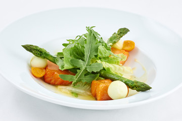 Delicious salad. Dish with pieces of grilled salmon, cheese, orange tomatoes, green leaves of arugula and asparagus on a white plate.