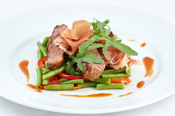 Delicious meal. Grilled beef with pork slices and boiled pepper, green beans, fresh arugula and sauce on a white plate.