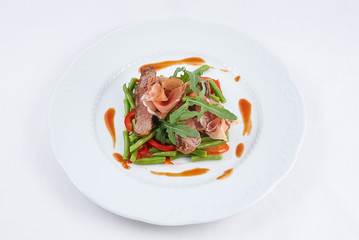 Delicious meal. Grilled tasty beef with pork slices and boiled pepper, green beans, fresh arugula and sauce on a white plate.