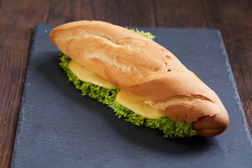 Fresh and tasty sandwich with cheese and vegetables on cutting board over wooden background, selective focus.