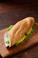 Fresh and tasty sandwich with cheese and vegetables on cutting board over wooden background, selective focus.