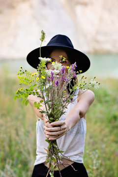 Giovane donna sorridente all'aperto nella natura nascosta da un bouquet di fiori di campo 