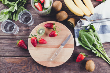 Preparing smoothies from spinach, banana, kiwi and strawberries on a wooden background