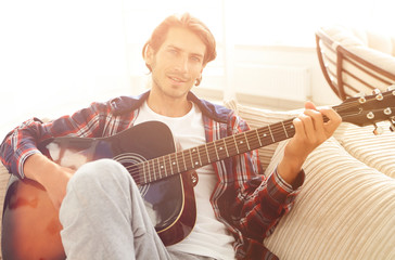 modern guy with guitar sitting on sofa in living room.