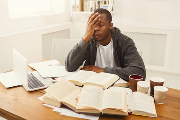 Black male student studying at table full of books