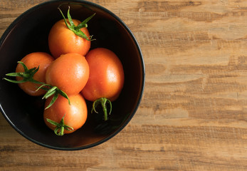 Orange tomatoes in a white bowl on wood background, with space for text