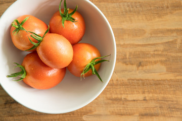 Orange tomatoes in a white bowl on wood background, with space for text