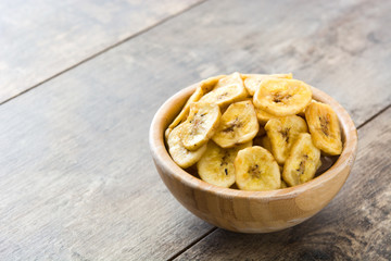 Banana chips in bowl on wooden table. Copyspace